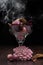 Glass filled with brown, pink and red potpourri with smoke on wooden table with black background. Rembrandt lighting inspired