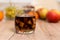 A glass filled with sugar cubes and a glass with cola are standing on the table. In the background, mandarin fruits, apples and gr