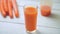 A glass of fresh carrot juice revolves around its axis on white wooden table