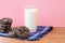 Glass of fresh milk with a pile of crunchy baked chocolate sugar cookies on wooden table with dark blue dinner napkin on pink back