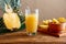 Glass of fresh natural pineapple juice with metal reusable tube on brown wooden table with ingredients. Fruit Pineapple
