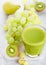 Glass of fresh smoothie organic green toned fruit on white chopping board on stone kitchen background. Pear and grapes with kiwi