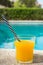 Glass of Freshly Pressed Tropical Fruits Orange Juice with Striped Straw on Deck of Villa Swimming Pool on Sunny Summer Day