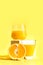 A glass of freshly squeezed refreshing orange juice on a white pedestal or podium with orange halves. Yellow background. The