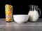 A glass full of colorful sugary cereals with a milk jug and a white ceramic bowl