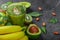 Glass full of green juice, kiwis, bananas and avocados on a stone table background. Close-up of fresh tropical fruits.