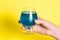 Glass goblet with blue liquid on a yellow background. A woman celebrates the completion of an important business, the beginning of