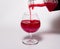 Glass goblet with red drink on a white background. With a splash of liquid from the bottle.