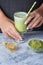 Glass with green latte. Matcha green tea and soy milk drink. Hands of a girl holding a glass, cropped photo
