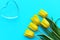 Glass heart and yellow tulips on a turquoise background, fragile love background, valentines day concept
