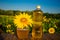 Glass honey jar and bottle of oil on wooden stand with sunflowers field background.