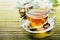 Glass of hot herbal tea on bamboo background closeup. Teacup with organic green tea and fresh jasmine flower on wooden table