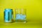 A glass of ice cubes sitting next to a can of lemonade over blurry background