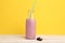 Glass jar with blackberry smoothie on a wooden surface and yellow background