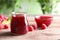 Glass jar and bowl of sweet jam with ripe raspberries on wooden table against blurred background.