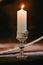 Glass jar candle burning brightly on a wooden table in a dimly lit room.