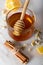 Glass jar full of honey and dipper with dried camomile herb tea, lemon and cinnamon sticks.