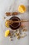 Glass jar full of honey and dipper with dried camomile herb tea, lemon and cinnamon sticks.