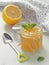 Glass jar full of lemon curd with cute spoon and meant leaf upon rustic table.