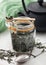 Glass jar of organic loose green tea with vintage metal strainer infuser on light board with Japanese Iron Teapot and green cloth