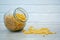 A glass jar with pasta scattered on a wooden table against the background of a white loft.