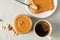 Glass jar with peanut butter, peanut, cup of coffee, spoon and peanut butter sandwich on grey background, top view