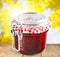 Glass jar with raspberry jam on background