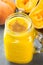 Glass jar with raw vegan pumpkin butternut squash smoothie with peaches, bananas, pie spices. Ingredients on dark stone background