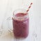 Glass jar with smoothie made of banana, black currant, coconut milk on a white wooden background, side view.