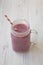 Glass jar with smoothie made of banana, black currant, coconut milk on a white wooden table, side view. Close-up