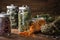 Glass jars of dry medicinal herbs - calendula, coneflowers, raspberry leaves and linden tree flowers, bunch of heather on table