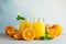 Glass jars with fresh orange juice and tubule, oranges and mint on white table against color background, space for text
