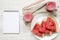 Glass jars of watermelon smoothie, top view. Slices on round plate, drinking straws and blank notepad on white wooden background.