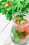 Glass Jug with Fresh Cool Infused Detox Water with Ripe Organic Strawberries Sliced Cucumbers Mint. White Plank Wood Background