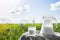 Glass jug with milk and a glass on the grass against a backdrop of picturesque green meadows with flowers at clear sunny summer da