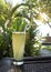 A glass of juice on the edge of the table on the street terrace, overlooking the pool and tropical plants. Indonesia, Bali