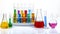 Glass laboratory materials such as erlenmeyer, tubes, and measuring cylinder containing colored liquids.Science chemistry concept