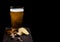 Glass of lager beer with snack on stone board on black background. Pistachios and pretzel with potato crisps. Space for text