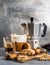 Glass of latte coffee on rustic wooden board, cantucci biscuits and steel Italian Moka pot, grey background