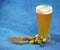 Glass of light wheat beer with foam, hops and ears of corn on a blue background