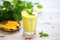 glass of mango lassi surrounded by fresh mangoes and mint leaves