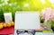 Glass of milk, blank page calendar, yellow fruit,sunglasses, pencils and pink flower on white wood table over green grass