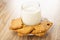 Glass of milk, muesli cookie in transparent saucer on wooden table