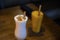A glass of milk shake with dry coconut on the top and mango smoothie with wooden straw for environment