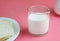 A glass of milk stands on a pink table, next to it lies bread in a white plate.