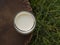 Glass of milk on wooden table, top view on green grass field