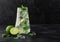 Glass of Mojito cocktail with ice cubes mint and lime on black board with fresh limes. Sparkling refreshing water