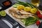 Glass mug with beer and fried smelts serving with vegetables, lime and sauces. Grey slate background. Top view