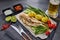 Glass mug with beer and fried smelts serving with vegetables, lime and sauces. Grey slate background. Top view