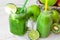 Glass mug with fresh green vegetable smoothie, bottle with fruit juice, apples, kiwi, lime,wood table outdoors, sunliht flecks